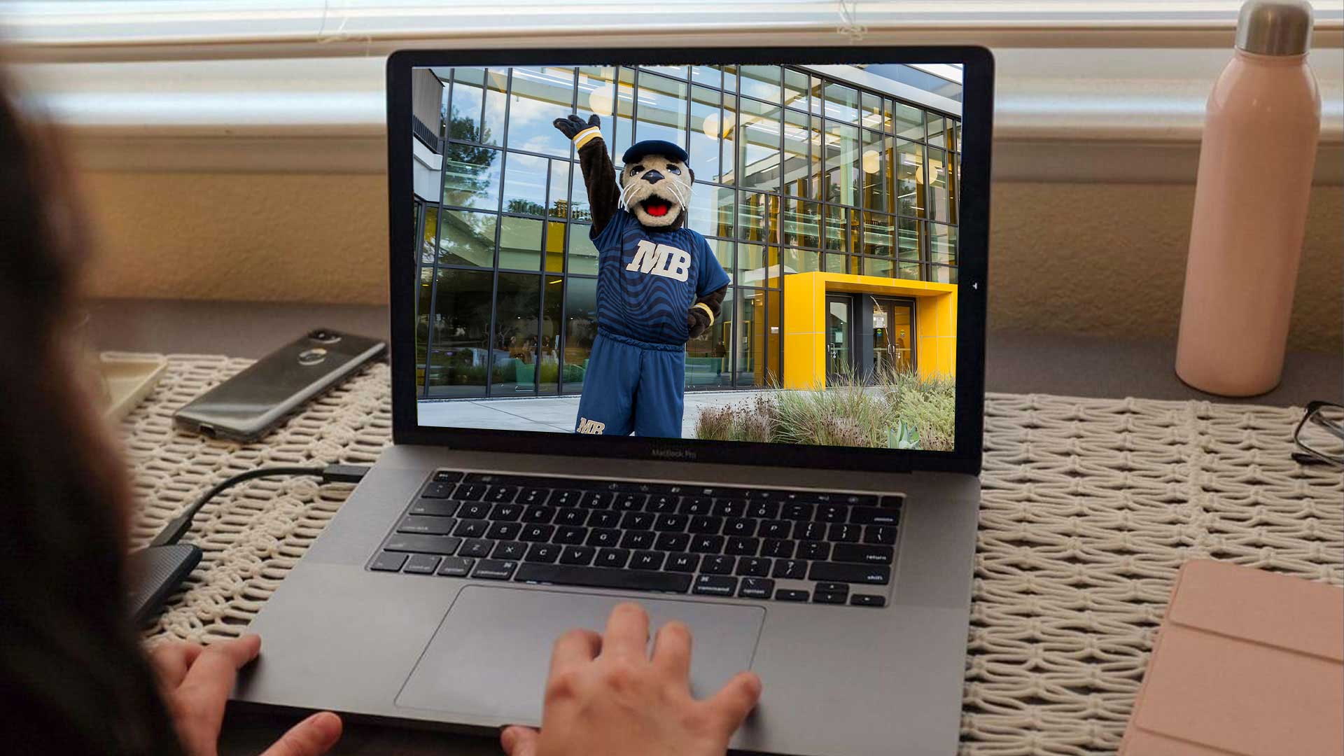 Photo: Student using laptop with picture of Monte on campus with arms out wide