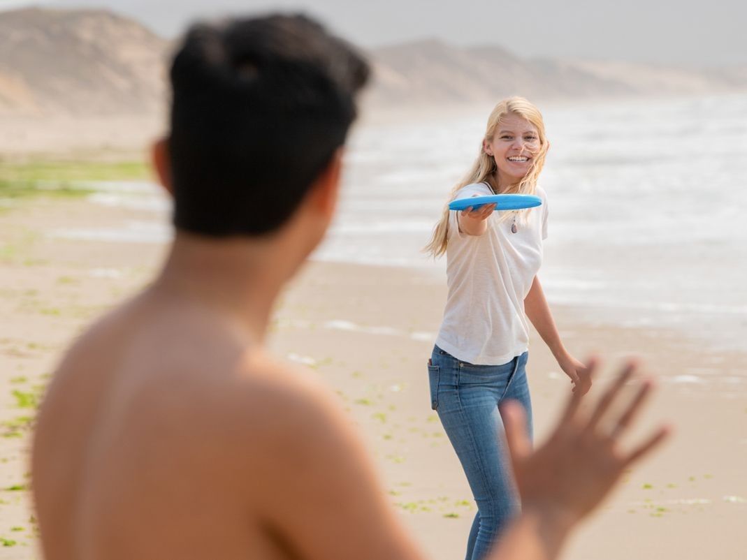 Two students playing frisbee on the beach