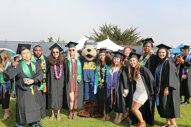 10 students in commencement regalia, grouped in a semi-circle with Monte