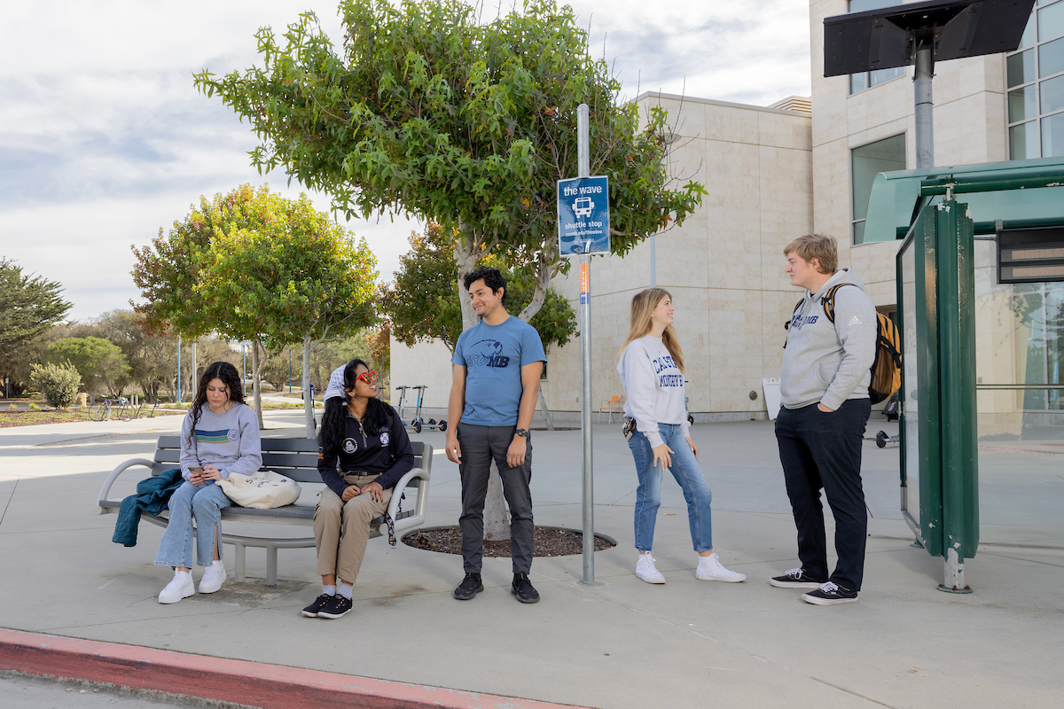 A group of students waiting at the bus stop for The Wave shuttle.