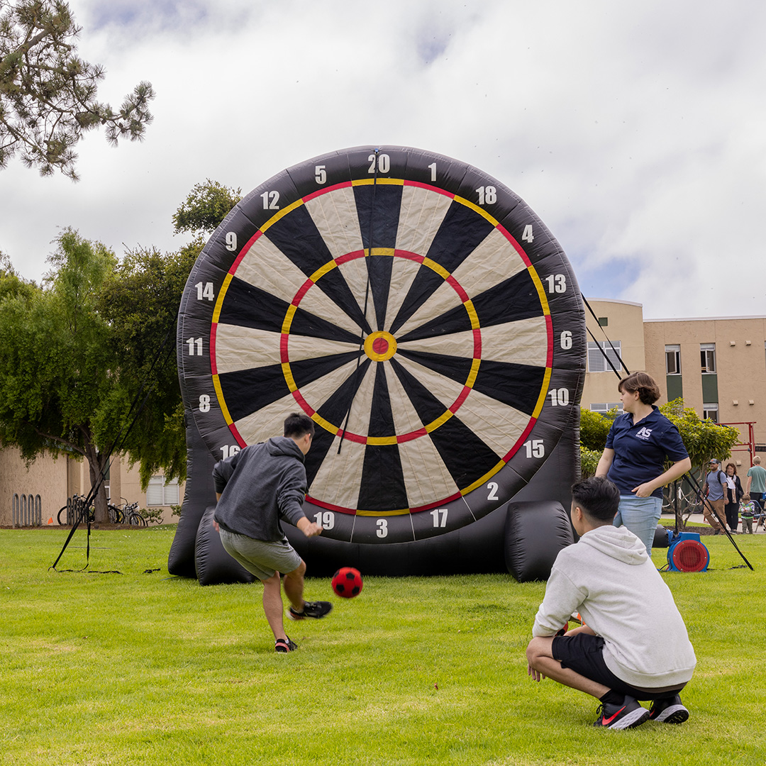 A student kicking a ball at a giant inflatable darts board.