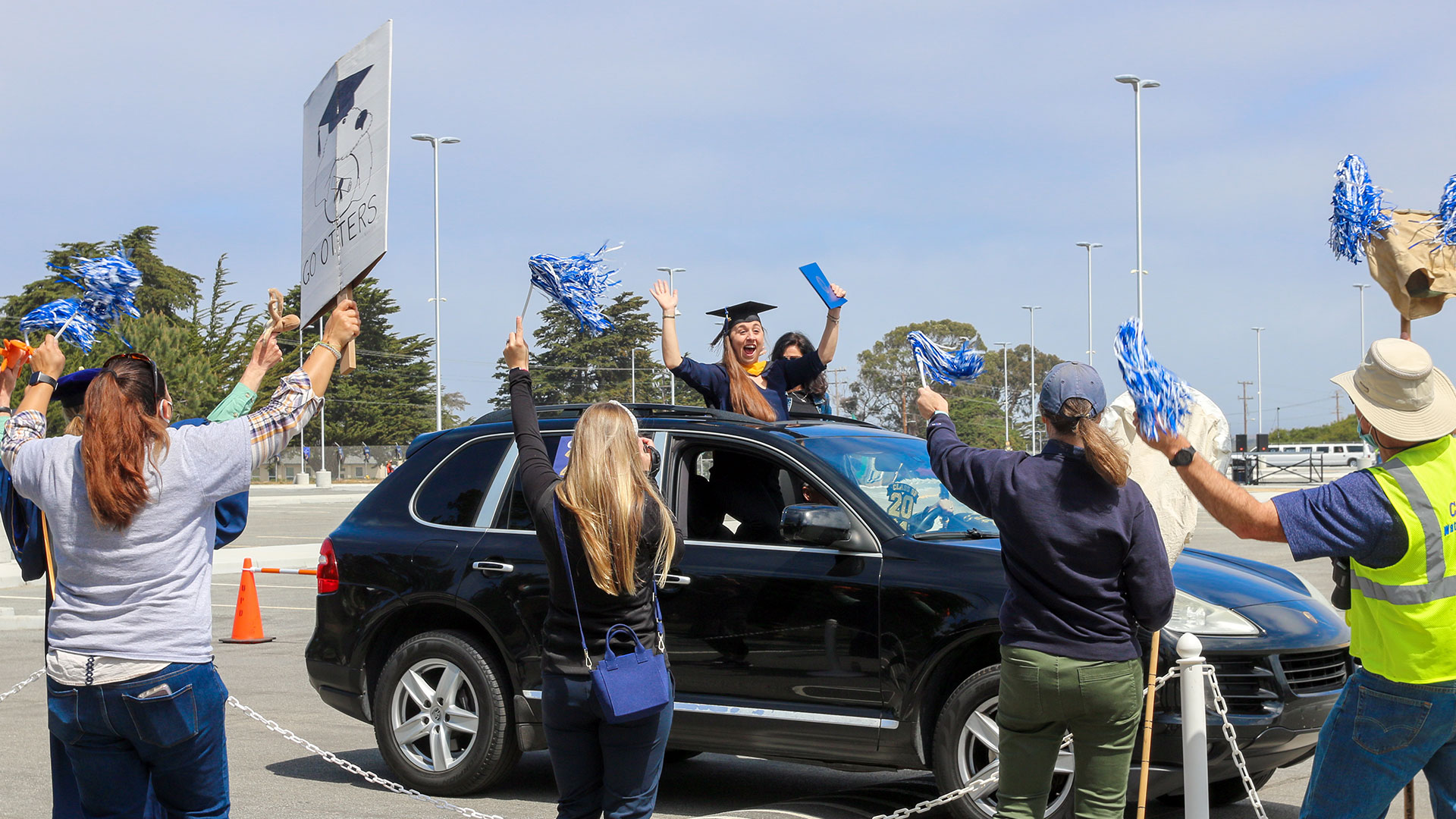 Excited graduate cheering from car while faculty and staff cheer her on