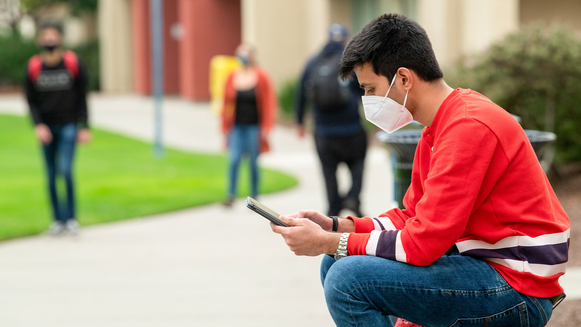 Photo: Masked student using a tablet with students in the background