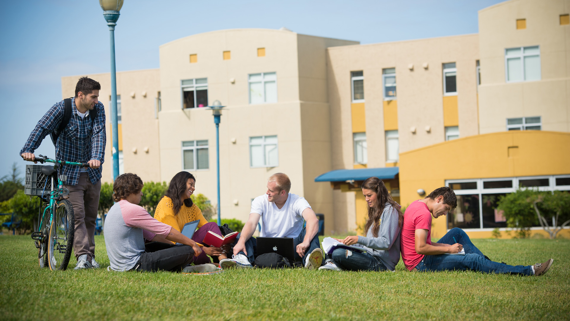 Five students sitting on the CSUMB Quad and one student holding his bike