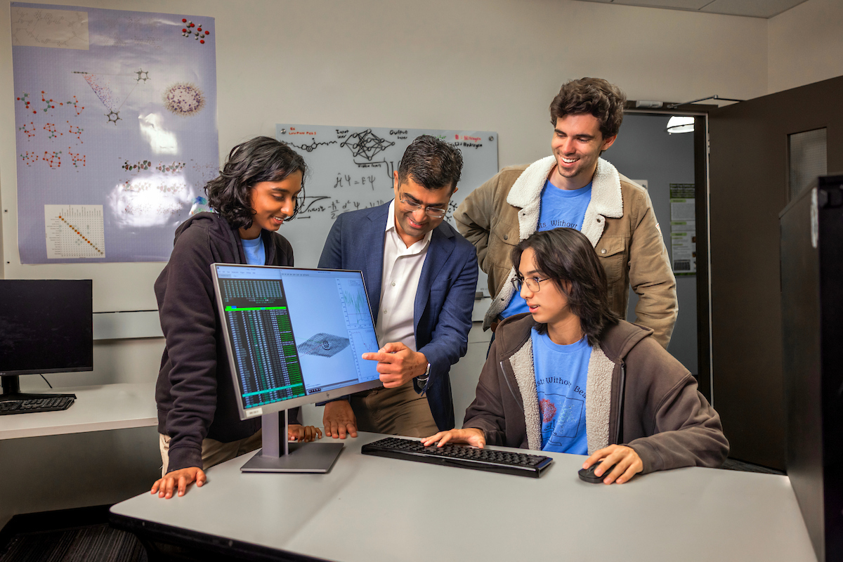 A group of three students and a professor huddled together looking at data on a computer screen