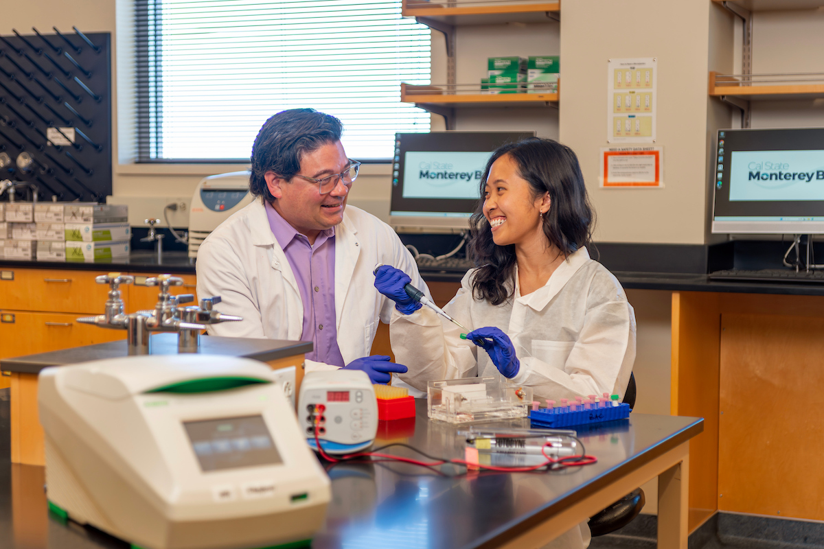 A professor and a student in lab coats looking at a syringe