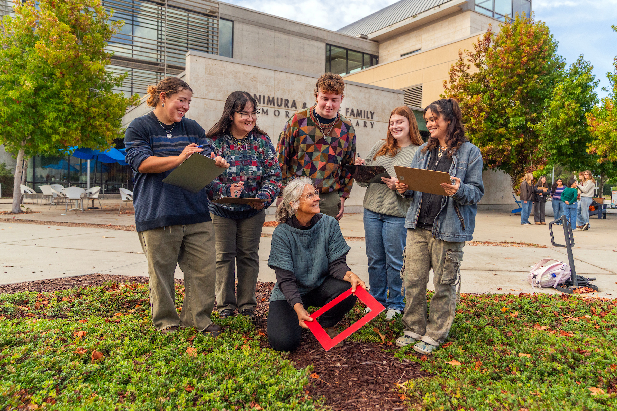 A CSUMB environmental studies instructor and students gather outside the library, recording observations and using a quadrat frame to study local plant communities.