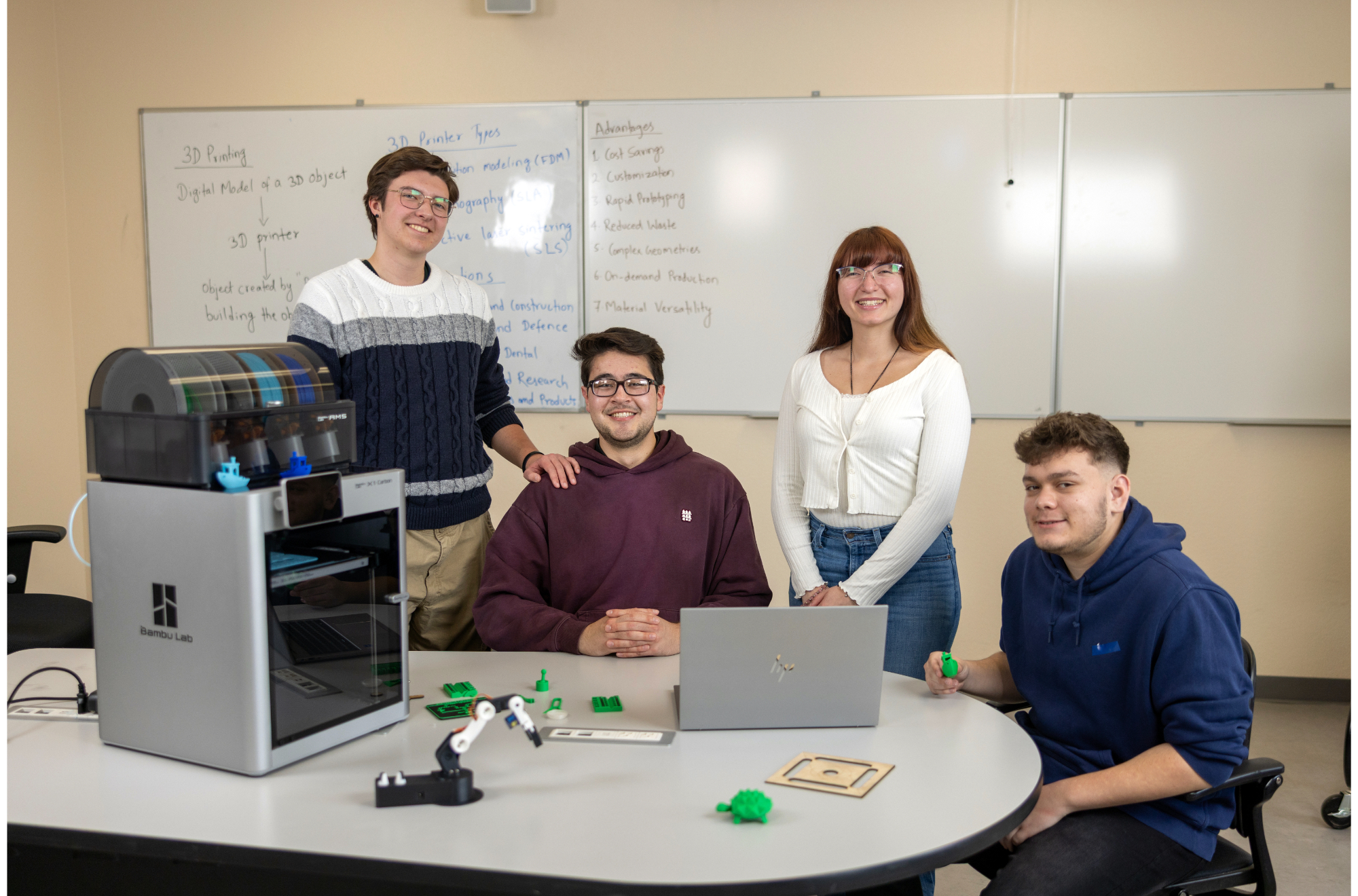 A group of four mechatronics students smiling at the camera next to a 3d printer