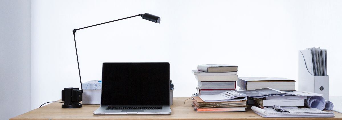 Photo of desk with laptop, textbooks, and paper work stacked.