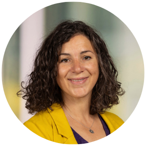 FYS Coordinator Headshot - Smiling woman with curly shoulder length hair in a mustard cardigan and black blouse