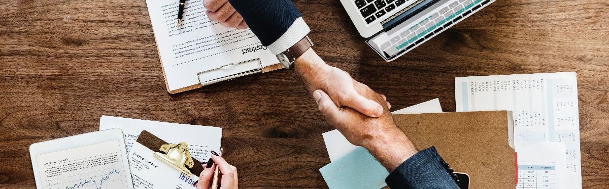 Photo of two hands shaking over desk with paperwork.