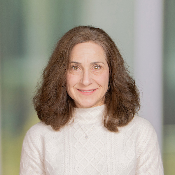 employee headshot of woman with long hair wearing white sweater in front of blurred background