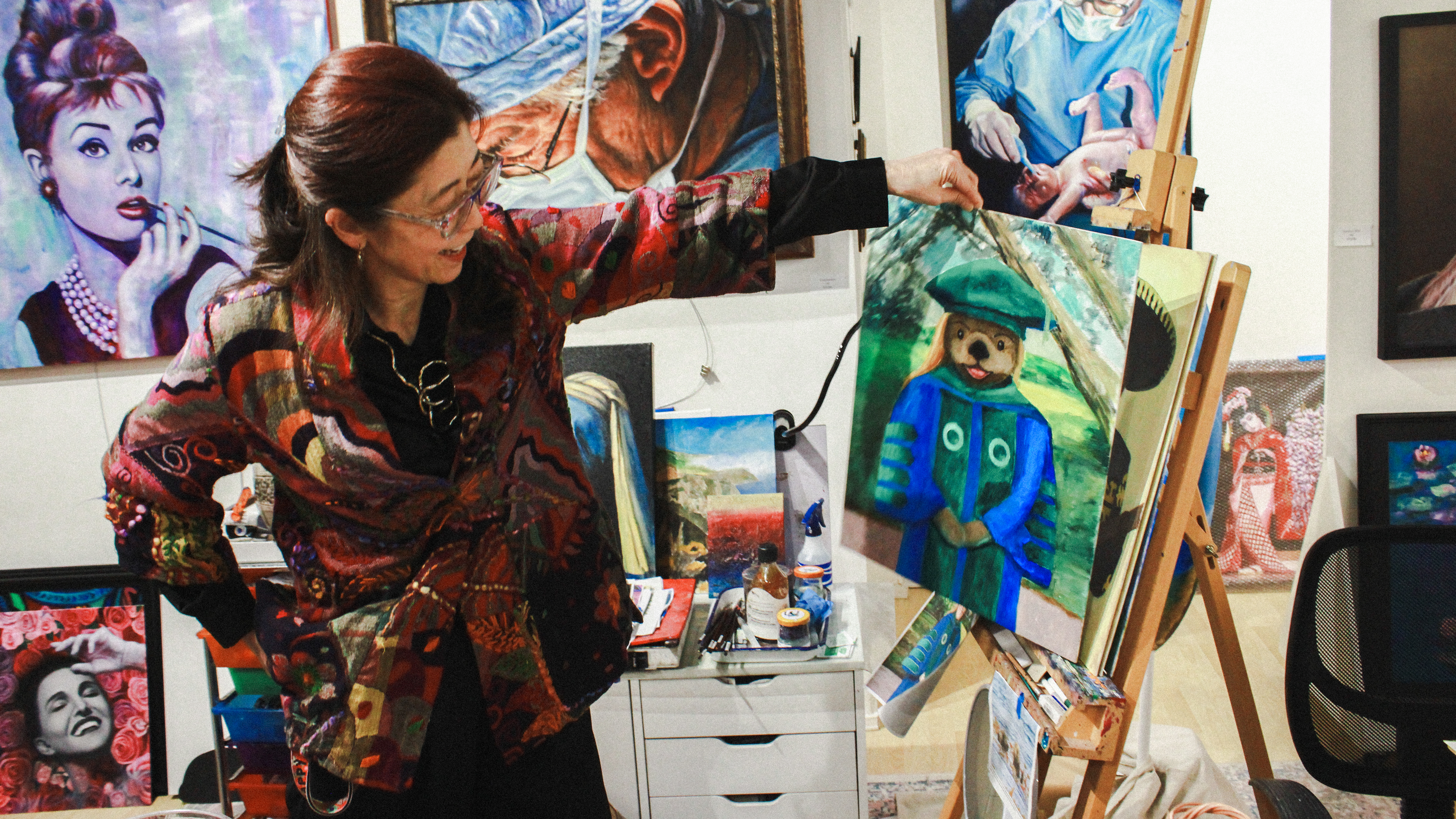 Artist Edi Matsumoto standing in her gallery, showcasing her artwork displayed on the walls behind her.