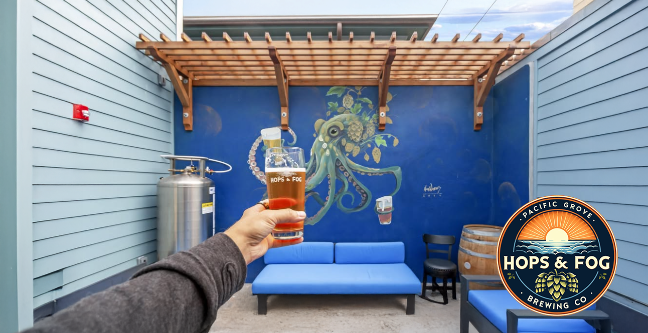 A hand holding a drink at Hops and Fog Brewery, with the Hops and Fog logo visible in the background.
