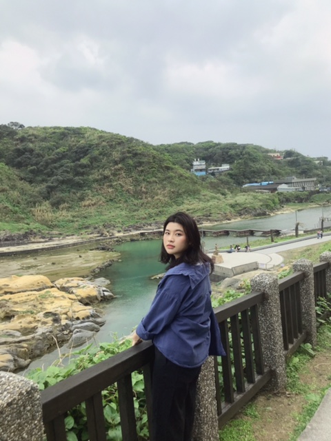 Ánh facing the camera while holding onto a railing. Behind Ánh is a river and hills