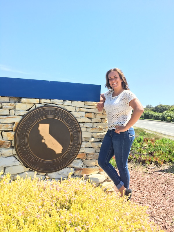 Brooke Fulkerson poses next to CSUMB emblem at the entrance to CSUMB