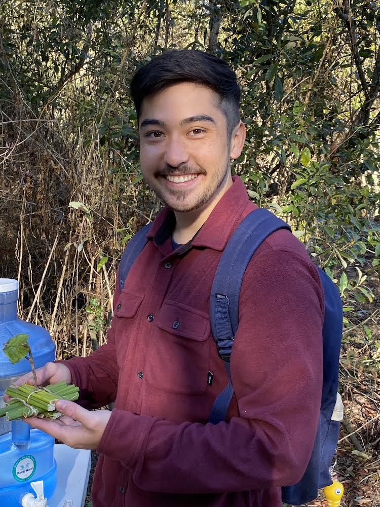 Nathan is smiling for the camera while holding a bundle of sticks