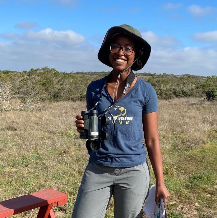 Student stands with binoculars in a grass field