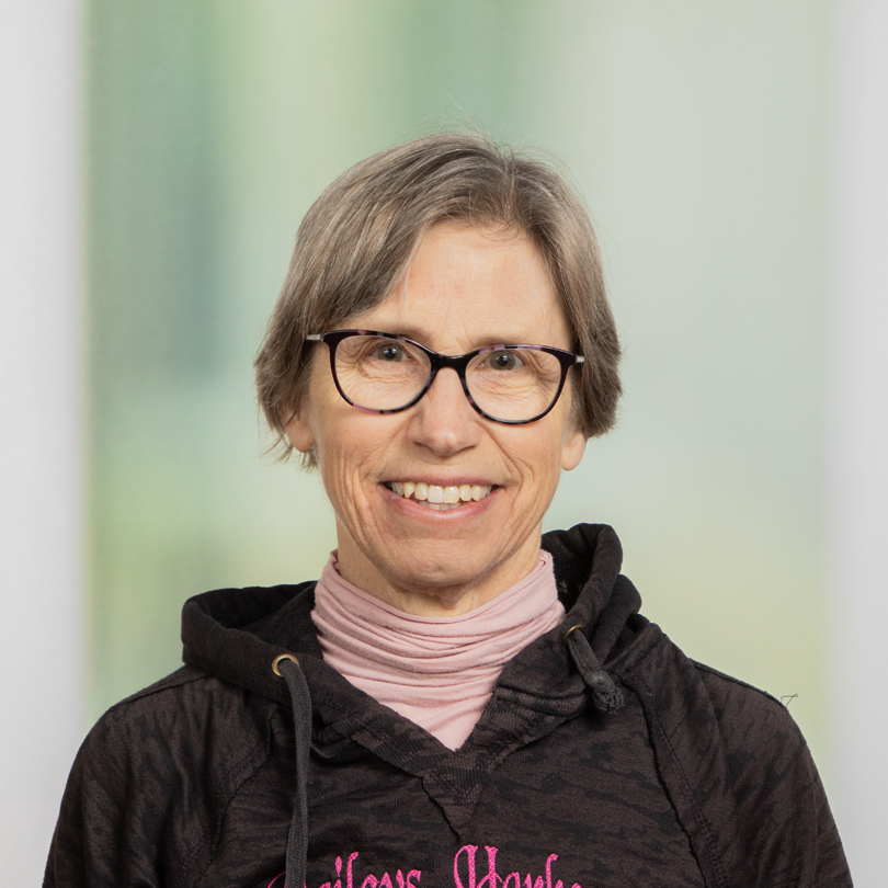 She is smiling and facing the camera. The background behind her is a blurred green