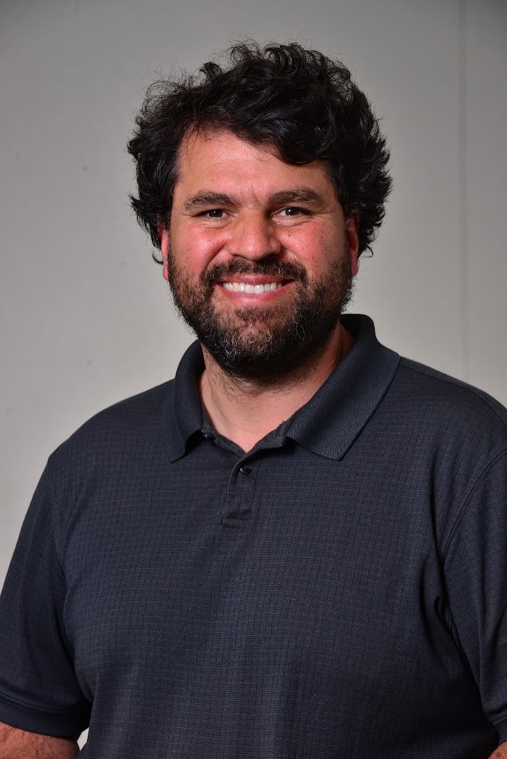 Gerick smiling at the camera wearing a dark gray polo shirt against a plain background.