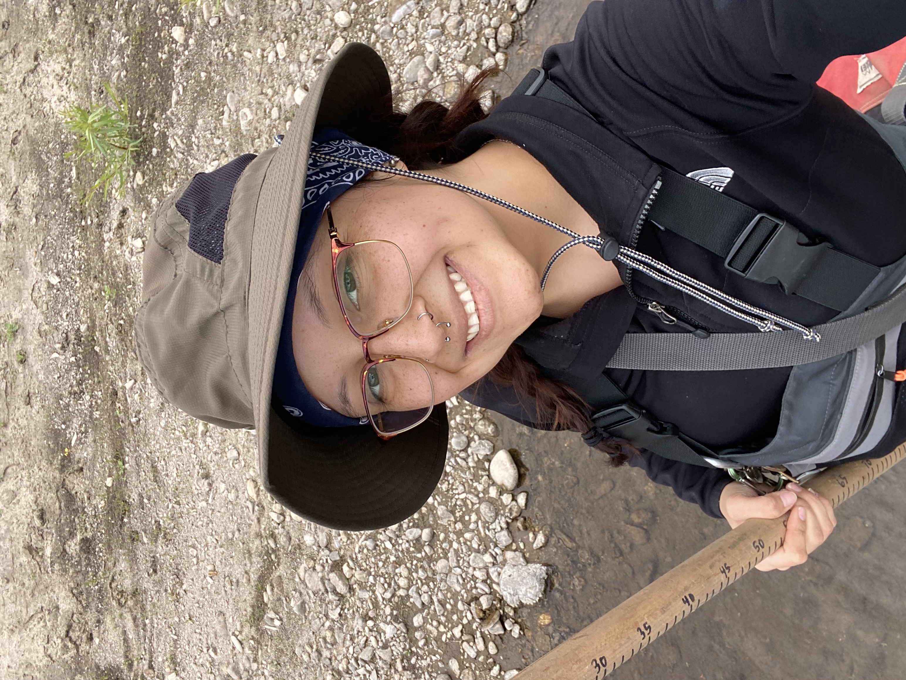 Savannah smiling for the camera. She's wearing a hat and carrying a hiking stick