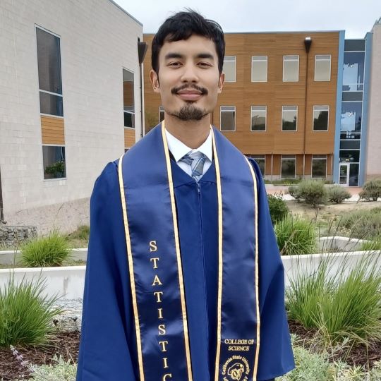 Graduate Nicholas Vasquez in regalia in front of Chapman Science Center