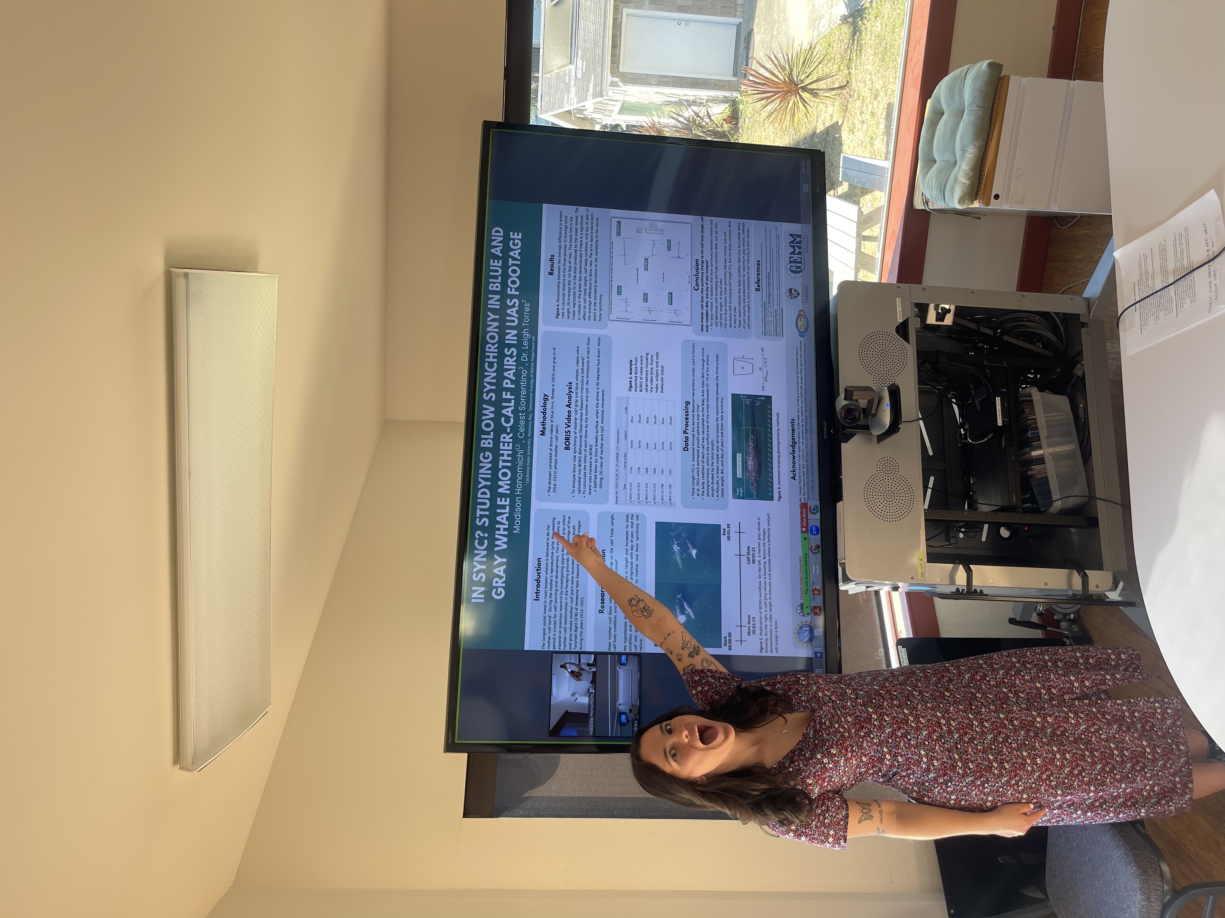 A woman enthusiastically points at a research poster on a large screen.