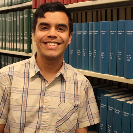 A Man standing by books smiling at the camera