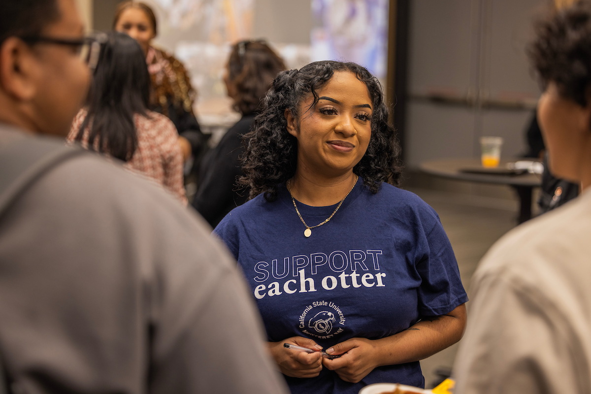 student with curly hair wearing a shirt that says support each otter