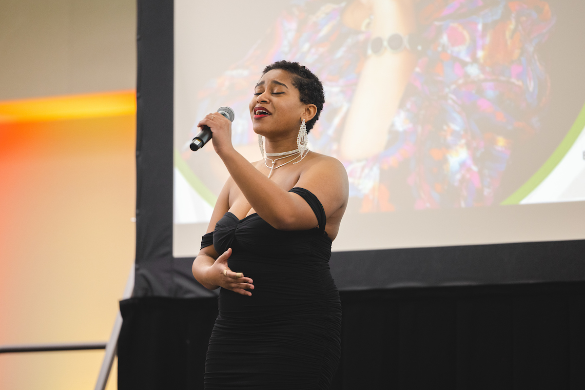 student wearing black dress singing into microphone