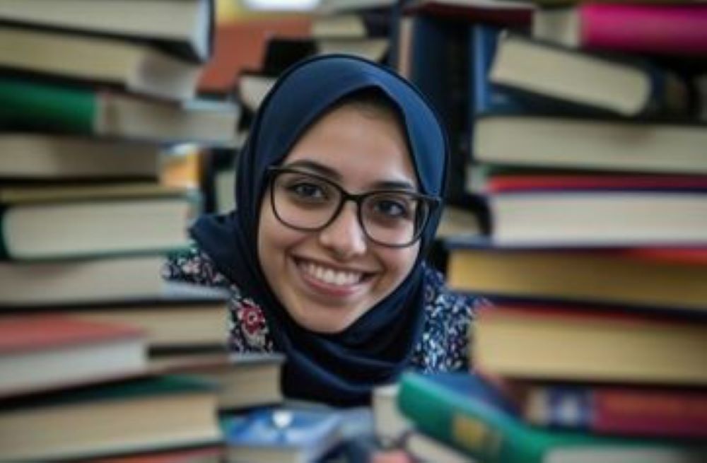 Person smiling through stacks of books.