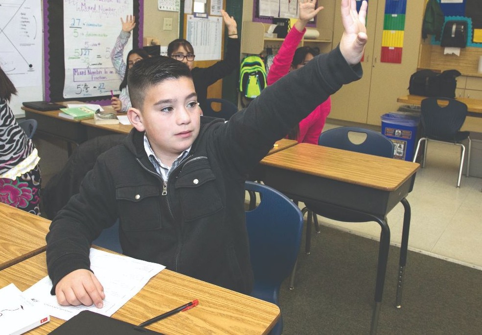 child at a desk raising his hand