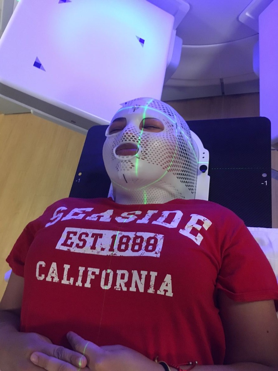 Sierra wearing a white mask, receiving brain cancer treatment.