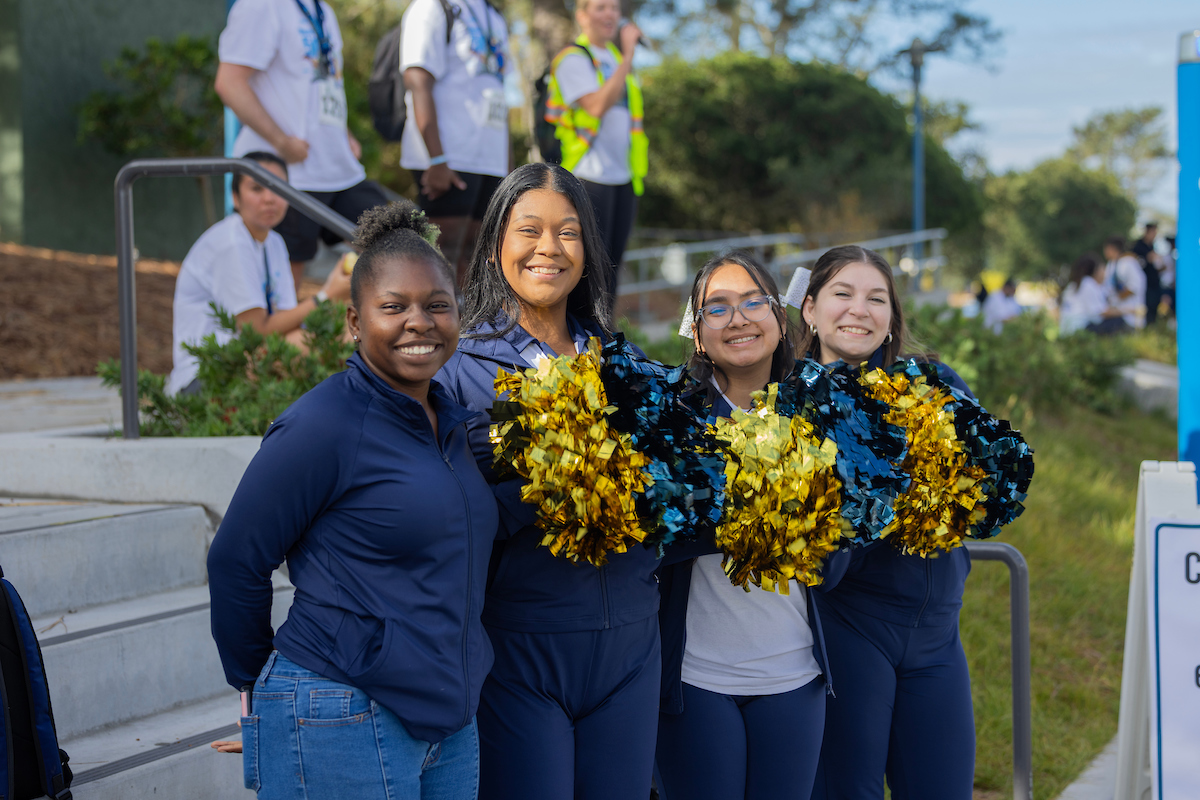 Four CSUMB students posing at Montes 5k event with blue and gold pom poms