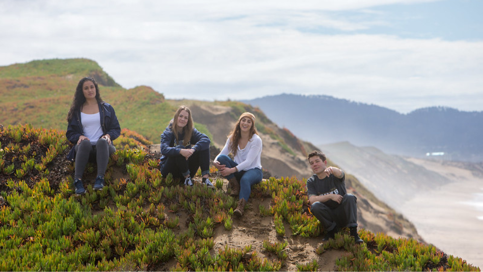 Students sitting on top of sand dune near the ocean