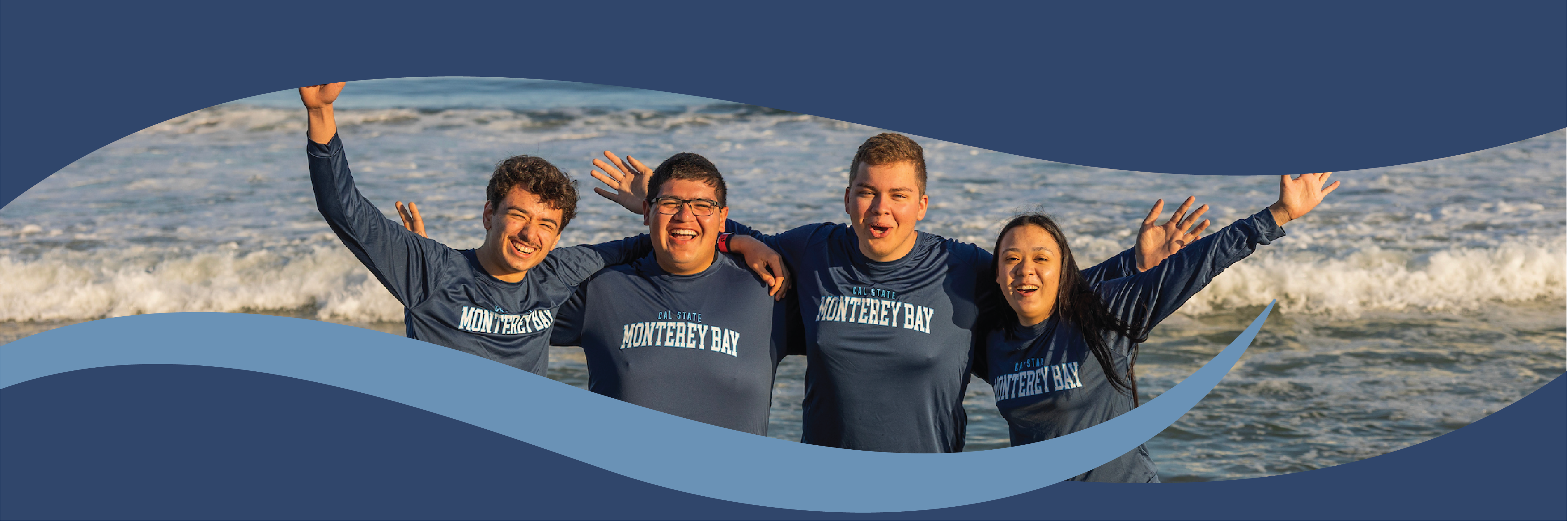 Four students in matching blue shirts on the beach.