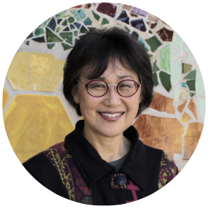 Woman with glasses and short black hair smiling in front of a mosaic art piece