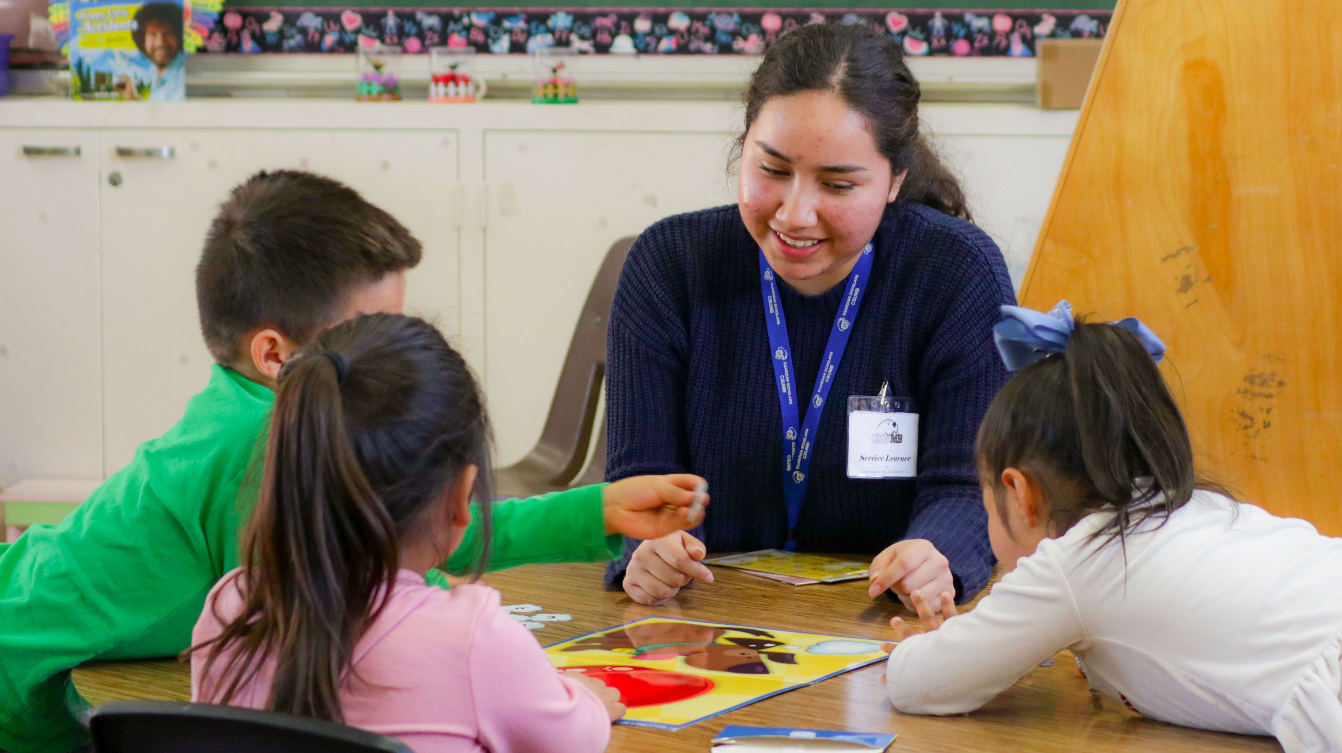 Student in a classroom with young children playing a board game