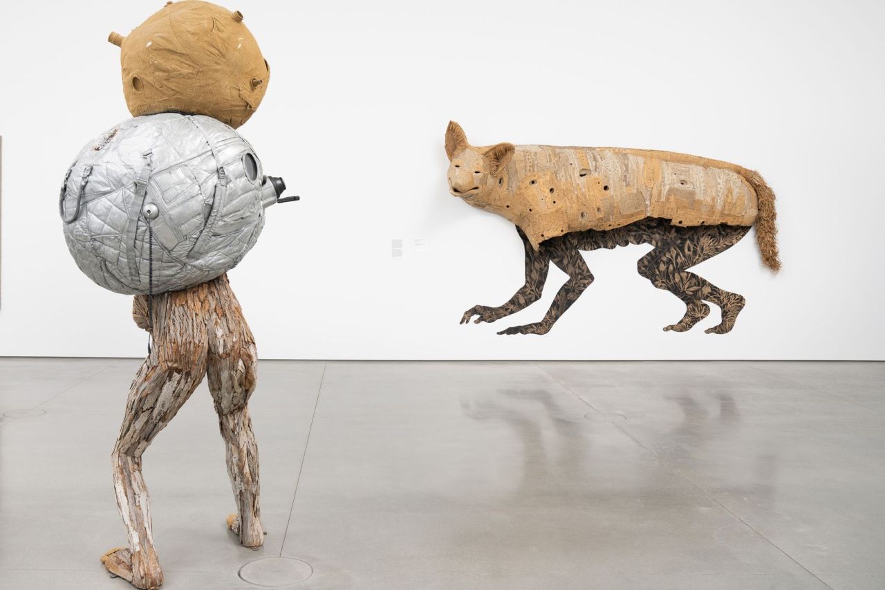 art installation man with bundle on back faces coyote