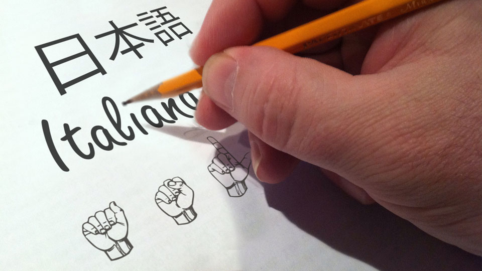 Photo: Hand holding pencil writing in different languages