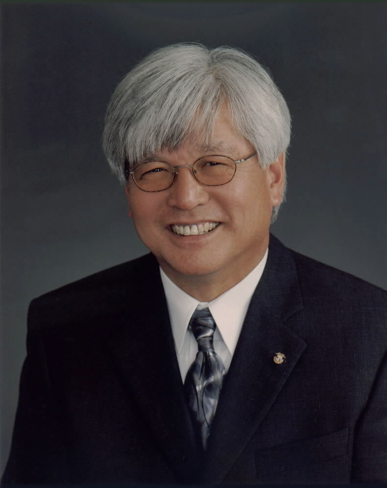 Smiling Larry Oda with white hair and glasses in dark suit and necktie
