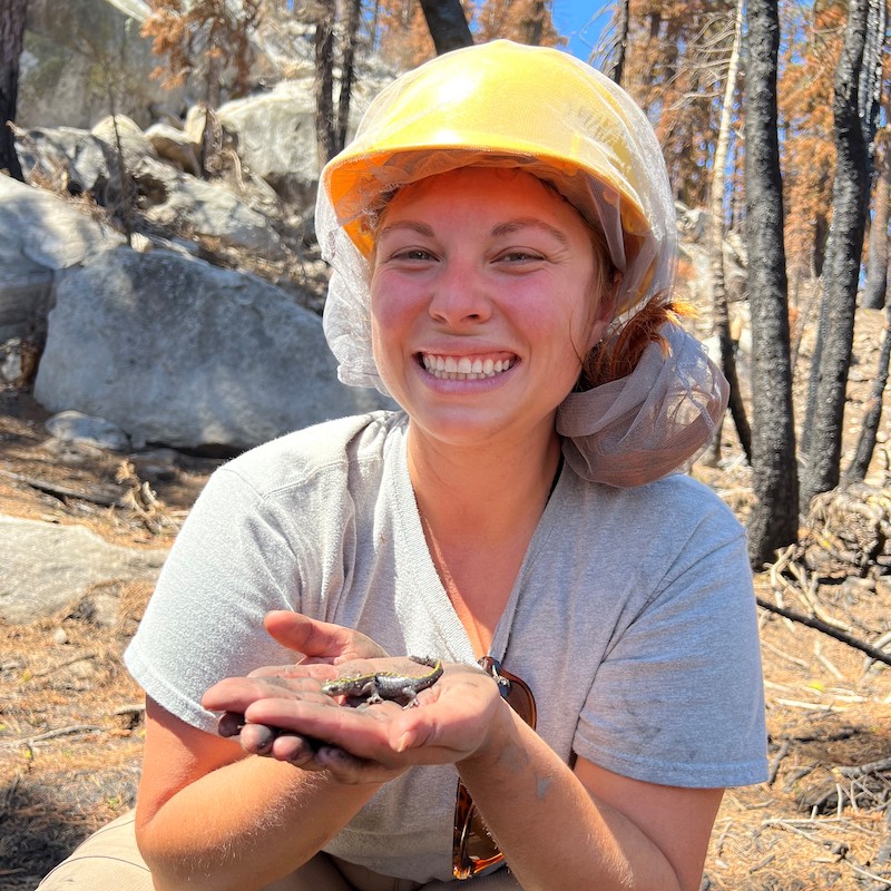 Erika poses with a small lizard in a her hand and a hard hat on