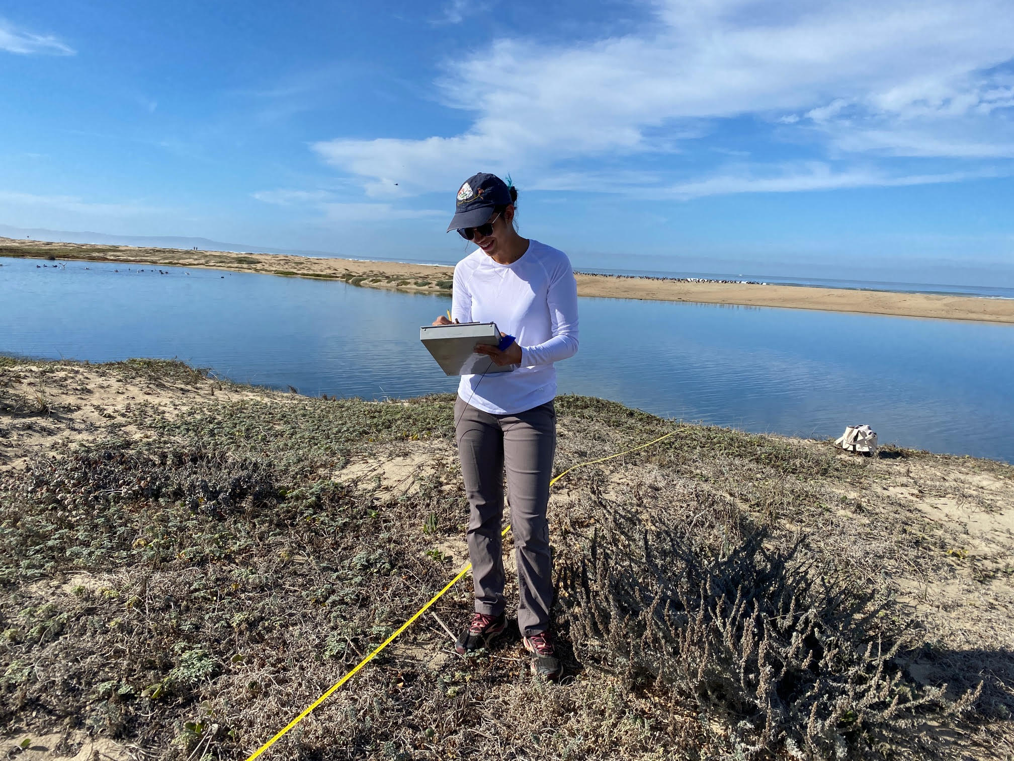 Aubrie stands in a wetland habitat while recording samples on a clipboard