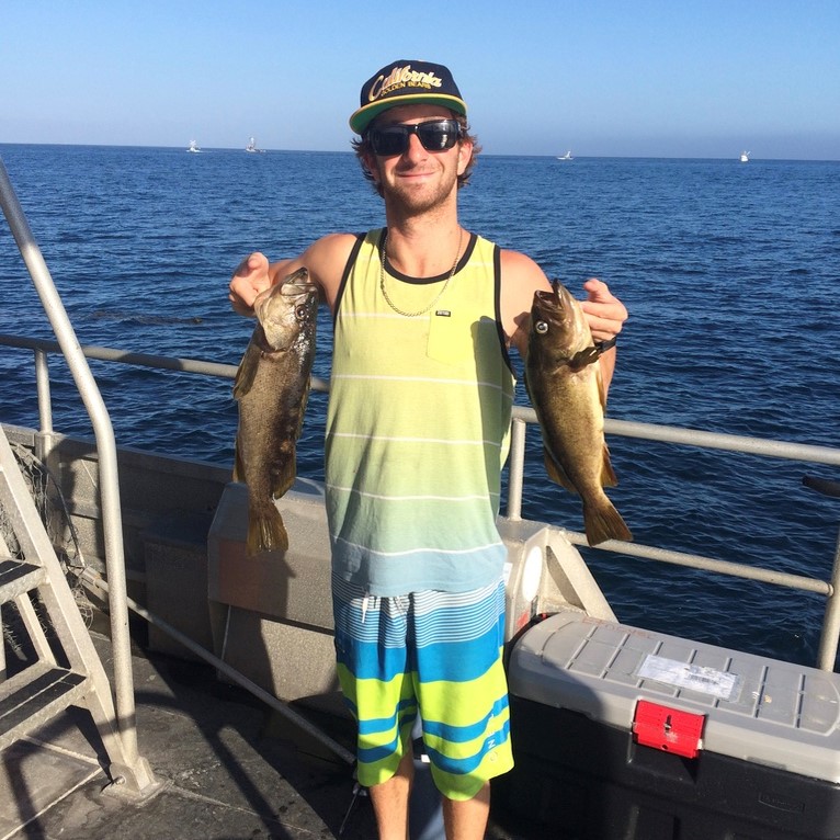 David Minovitz posing with two fish on a fishing boat