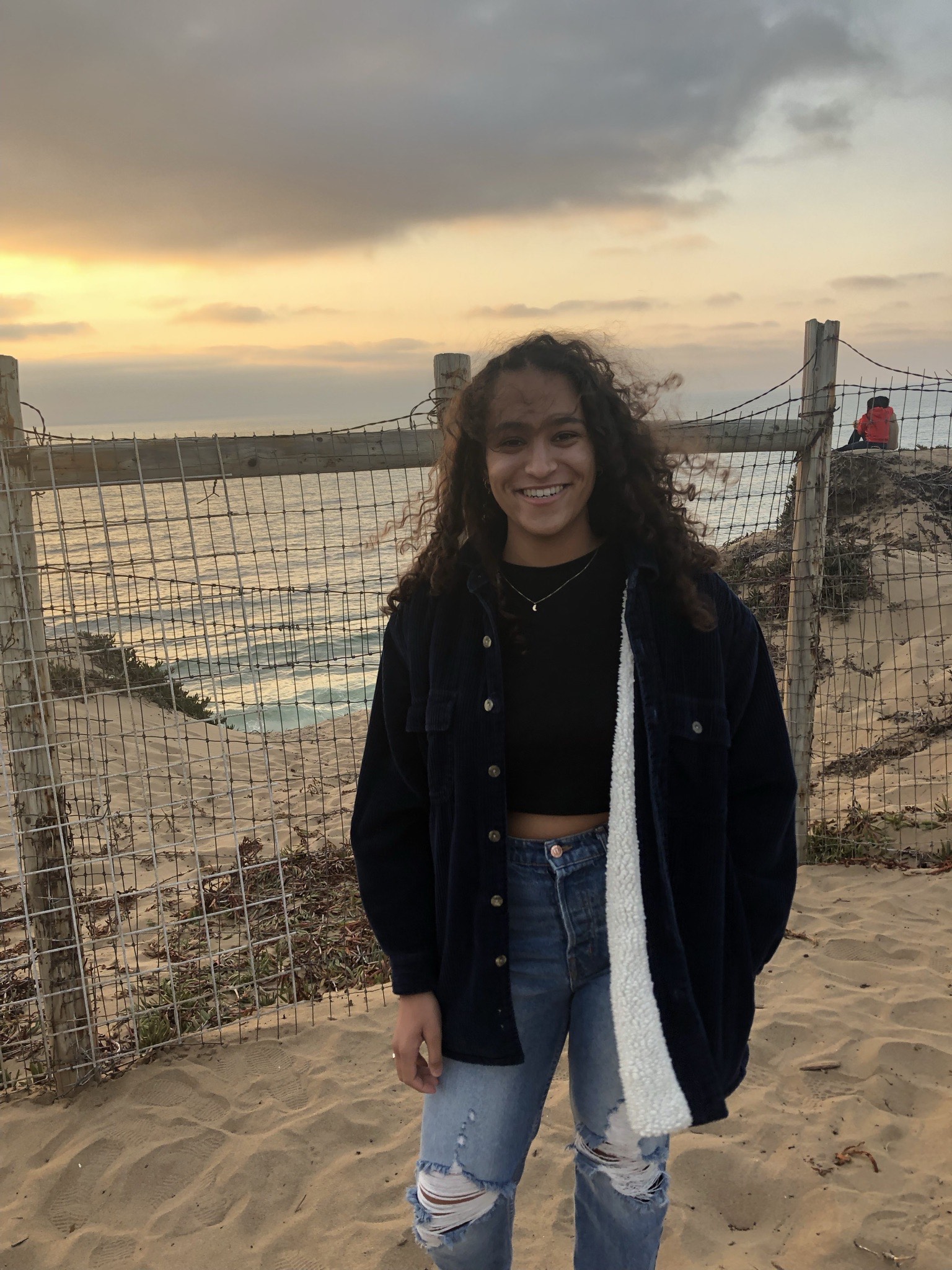 Annie smiling for the camera in front of a beach at sunset