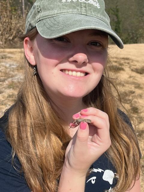 Person holding a small lizard outdoors, wearing a green cap.