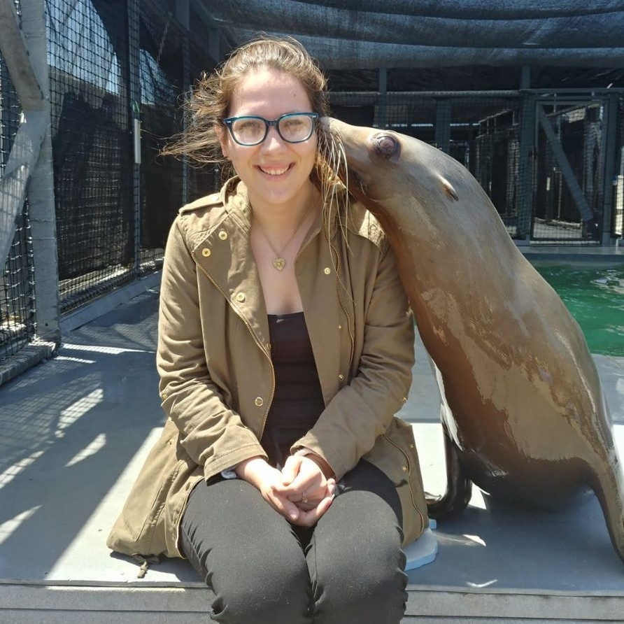 Student sits next to a sea lion who gives them a kiss on the cheek