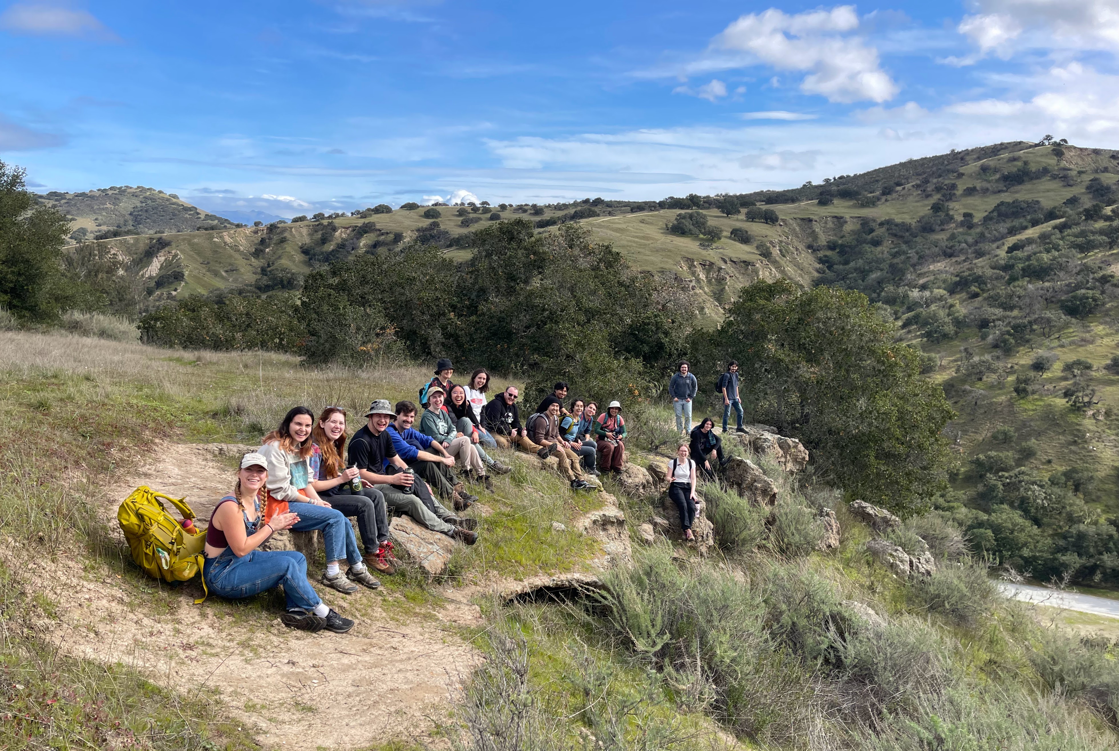 Students smiling and facing the camera while sitting on a hilly cliff