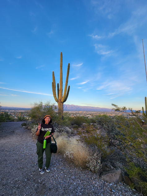 Elise smiling and posing for the camera. In the background is a tall cactus