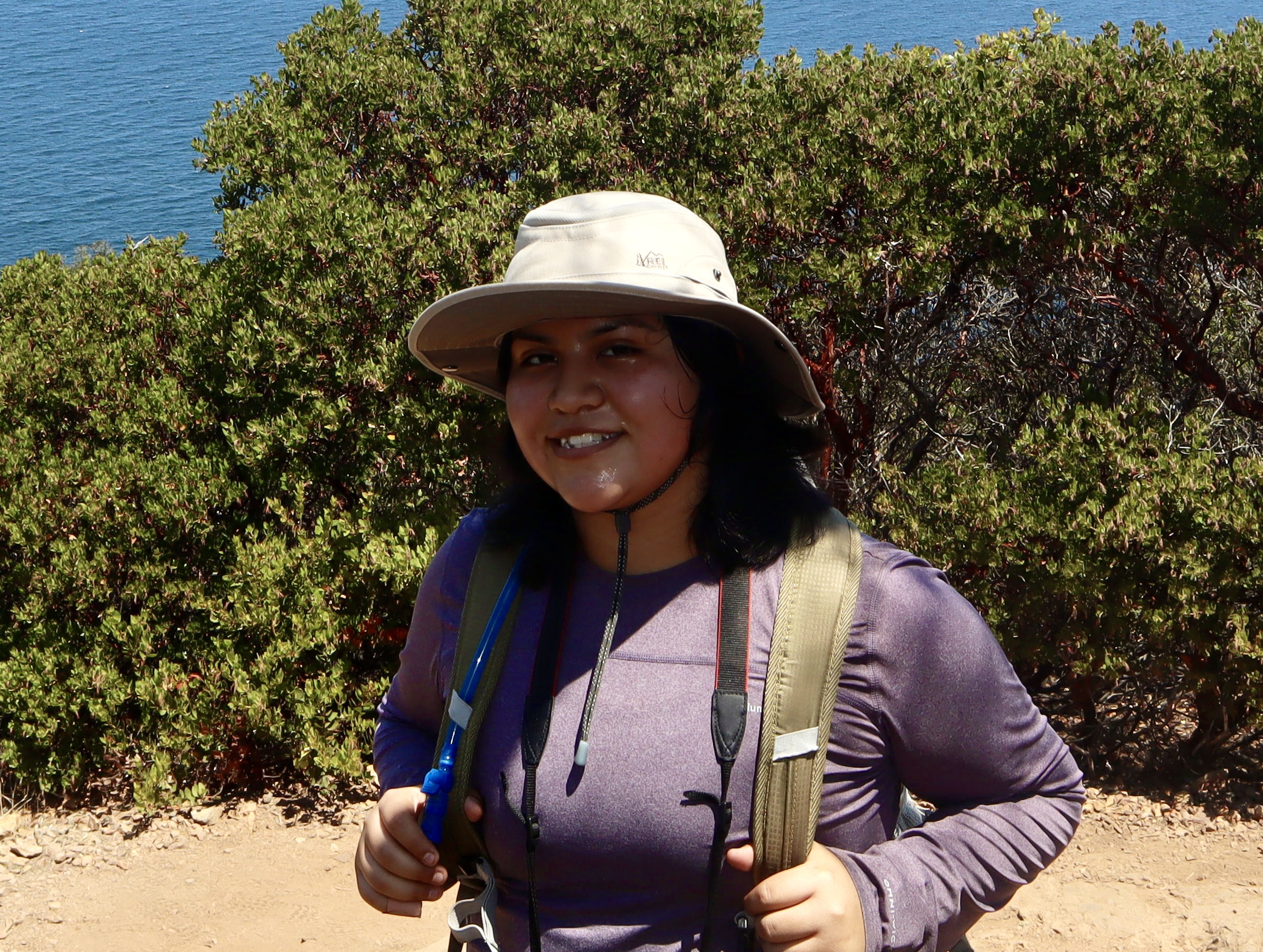 Marie smiling and posing for the picture. She stands near a bush